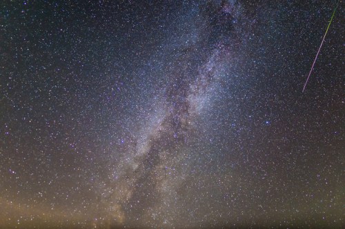 A stunning view of the Milky Way galaxy filled with stars, featuring a bright meteor streaking across the night sky.