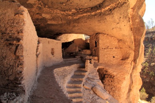 Ancient cliff dwellings with stone steps and a winding path, surrounded by rocky terrain and natural formations.