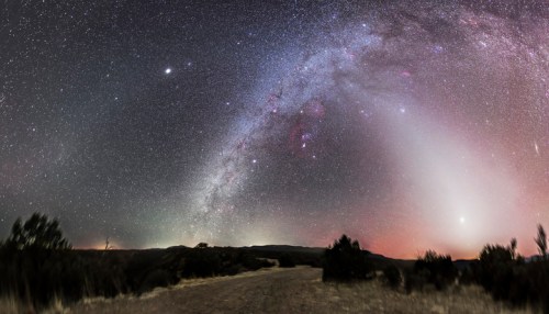 A panoramic view of a starry night sky with the Milky Way arching over a dark landscape.