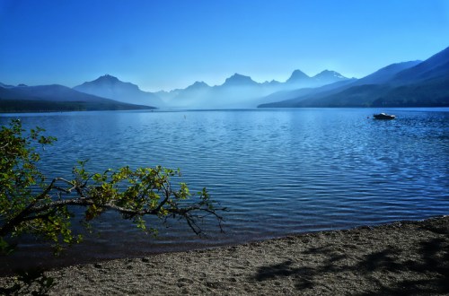 A serene lake surrounded by mountains, with a clear blue sky and gentle ripples on the water's surface.