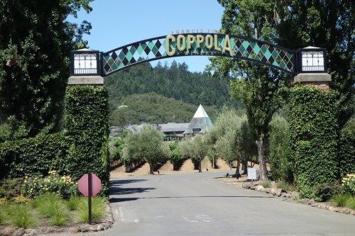 Entrance to Francis Ford Coppola Winery, featuring a decorative archway surrounded by greenery and vineyards.