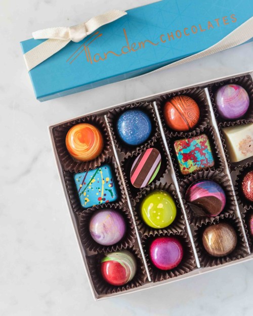 A colorful assortment of artisanal chocolates in a blue box, arranged in a grid with various designs and colors.