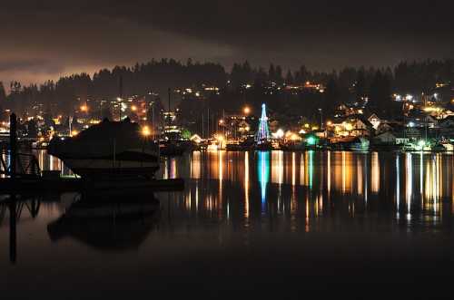 A serene night scene of a lake with boats, reflecting colorful lights from nearby houses and trees.