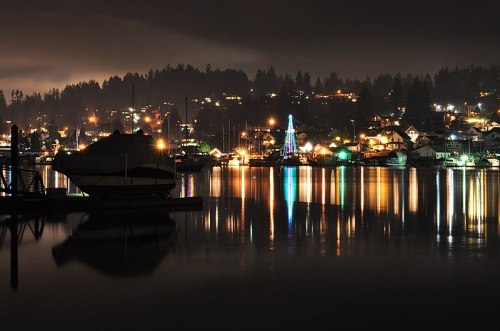 A serene night scene of a lake with boats, reflecting colorful lights from nearby houses and trees.