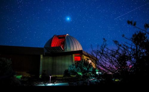 A dome observatory under a starry night sky, illuminated by red light, with a bright comet visible above.