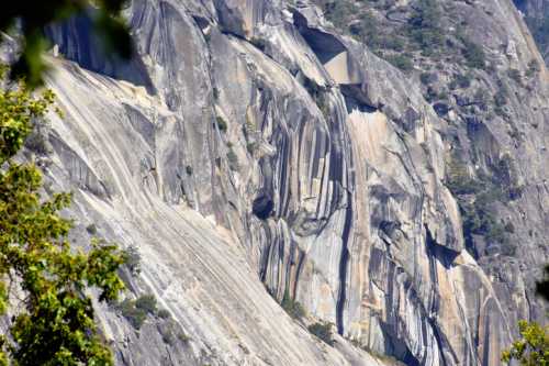 Close-up of a rugged mountain face with smooth, layered rock formations and patches of greenery.