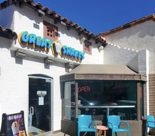 Exterior of "Great Shakes" shop with colorful signage, outdoor seating, and a clear blue sky.