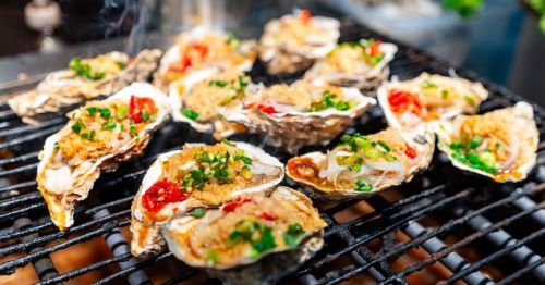 close up of oysters on the grill covered in various herbs, spices, and seasonings