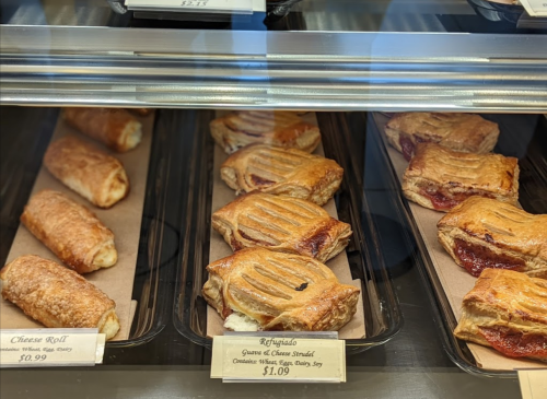 A display case filled with various pastries, including cheese rolls and fruit-filled strudels, with price tags visible.