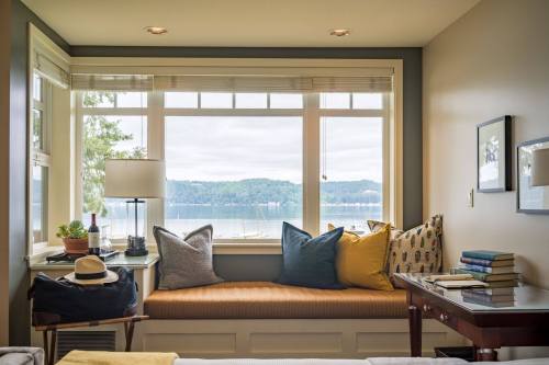 Cozy nook with cushions, a view of a lake, and a small table with books, creating a serene reading space.