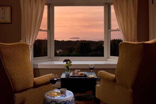 Cozy room with two armchairs, a table with snacks, and a sunset view over the ocean through large windows.