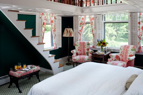 Cozy bedroom with floral decor, a staircase, and a sunny window view, featuring a small table with breakfast items.