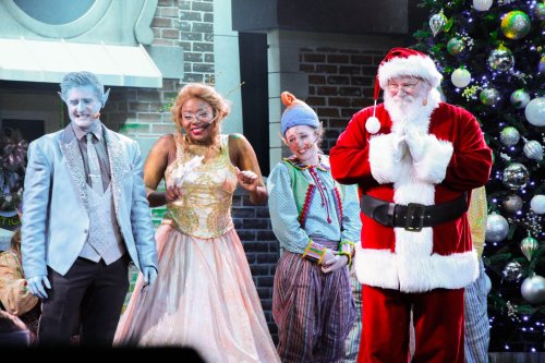 A festive scene with Santa and three performers in colorful costumes, celebrating in front of a decorated Christmas tree.