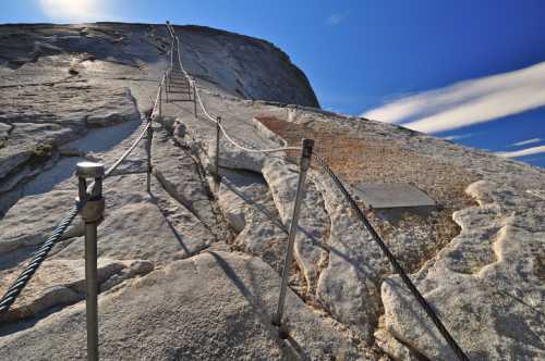 A steep granite slope with metal cables for climbing, under a clear blue sky.