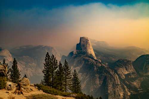 A scenic view of a mountain peak surrounded by trees, with a hazy sky and distant mountains in the background.