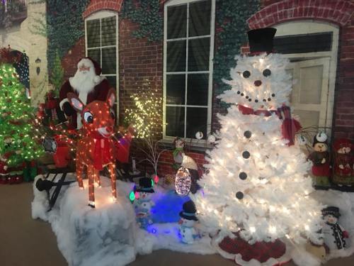 A festive scene featuring Santa, a lit reindeer, a snowman, and a decorated Christmas tree with colorful lights.
