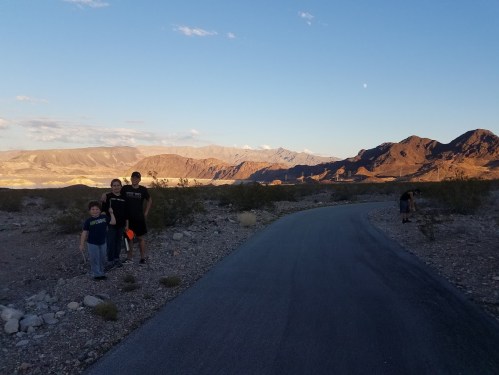 A family stands on a path in a desert landscape with mountains in the background under a clear blue sky.