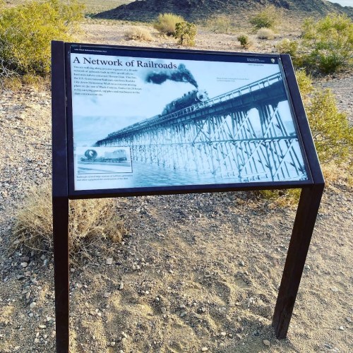 Sign about railroads with a historical photo of a train on a bridge, set in a desert landscape.