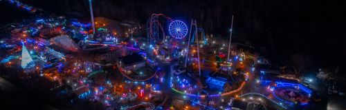Aerial view of a vibrant amusement park at night, illuminated with colorful lights and rides.