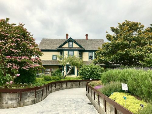 A charming house surrounded by lush gardens and colorful flowers under a cloudy sky.