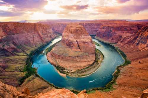 Aerial view of Horseshoe Bend, showcasing a winding river surrounded by red rock formations under a colorful sky.