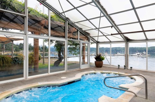 Indoor spa with a view of a lake and boats, surrounded by large windows and greenery.