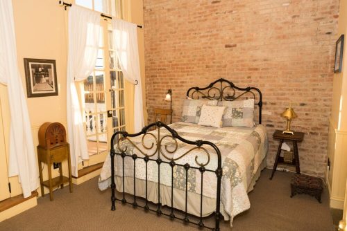 Cozy bedroom with a brick wall, a patterned quilt on a metal bed, and a bedside table with a lamp.