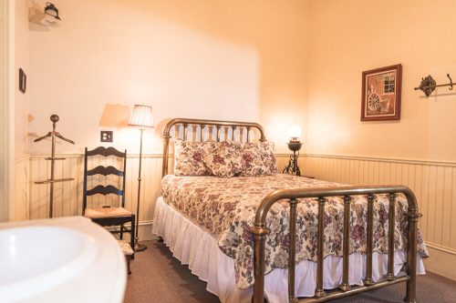 Cozy bedroom with a floral bedspread, vintage lamp, and wooden furniture in a softly lit, warm-toned room.