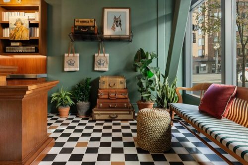 A stylish interior with a green wall, checkered floor, vintage suitcases, plants, and a wooden bench.