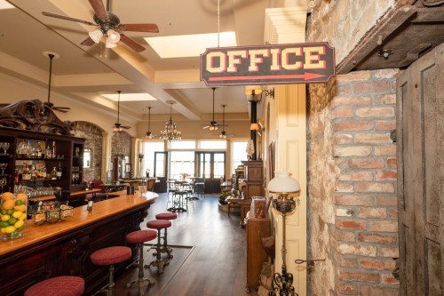 A rustic bar area with a sign pointing to an office, featuring wooden furniture and a warm, inviting atmosphere.