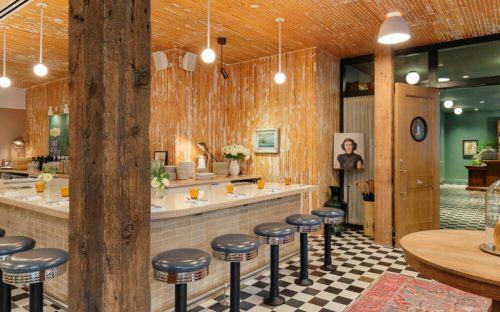 A stylish restaurant interior featuring a bar with stools, wooden beams, and vibrant orange walls.