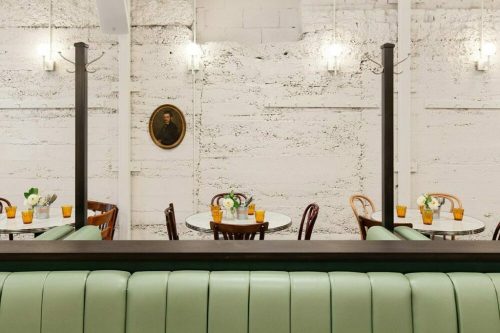 A modern café interior with green seating, round tables, and a vintage portrait on the wall.
