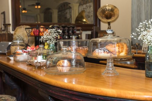 A wooden counter displays various pastries under glass cloches, with decorative flowers in small vases.
