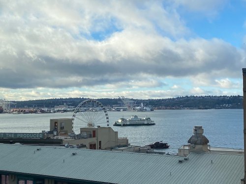 A view of a waterfront with a ferris wheel, a ferry, and clouds over the Seattle skyline.
