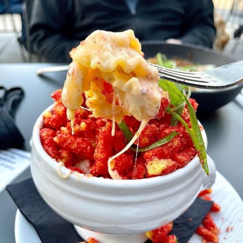 A fork holding cheesy pasta topped with crushed Cheetos and green onions, served in a white bowl.