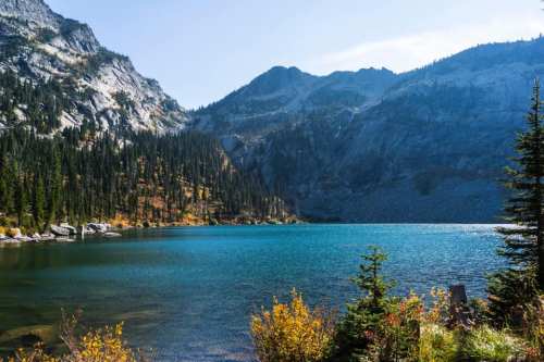 A serene lake surrounded by mountains and evergreen trees under a clear blue sky.