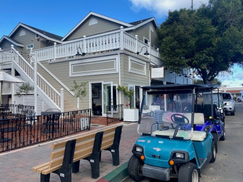 A blue golf cart parked near a two-story building with a white balcony and outdoor seating.