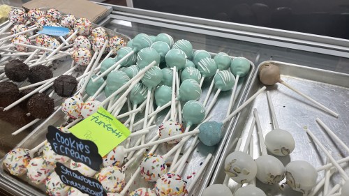 A tray of colorful cake pops in various flavors, including mint, cookies and cream, and chocolate, on display.