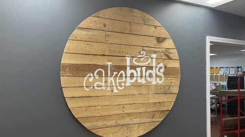 Wooden circular sign on a gray wall with the text "cakebids" in white.