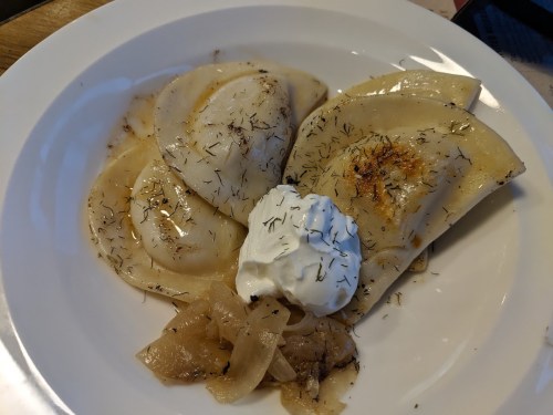 A plate of pierogi topped with sour cream and caramelized onions, garnished with herbs.