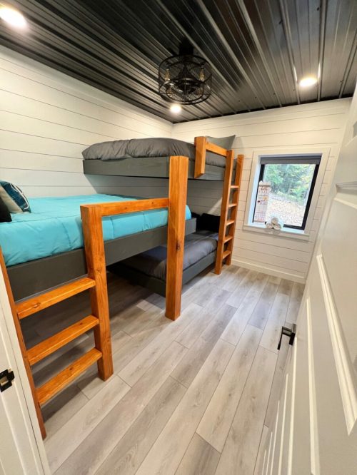 Cozy bedroom with a bunk bed, wooden ladder, and large window, featuring light wood flooring and a modern ceiling.
