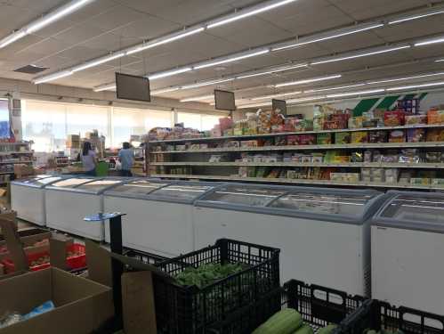 A grocery store aisle with freezers, shelves stocked with snacks, and shoppers in the background.