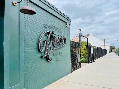 A green brick wall featuring a stylish sign that reads "Press Coffee Co." with a cloudy sky in the background.