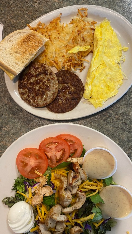 A plate with toast, hash browns, sausage patties, and an omelet; another plate with salad, grilled chicken, and dressing.