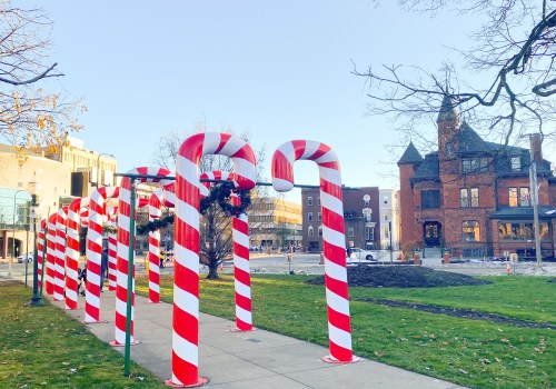 Large candy cane decorations line a pathway in a park, with a historic building visible in the background.