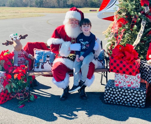 A child sits on Santa's lap outdoors, surrounded by festive decorations and a small Christmas tree.