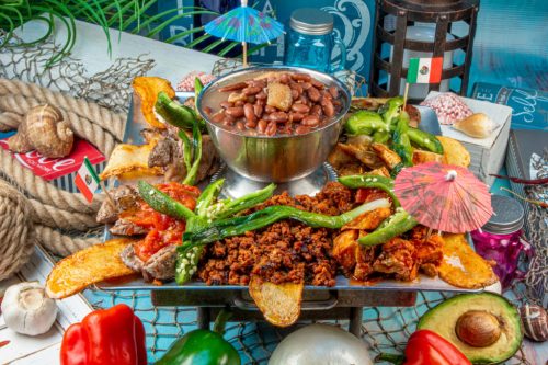 A vibrant platter featuring grilled meats, beans, fried plantains, and colorful garnishes, set against a festive backdrop.