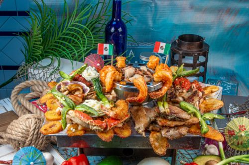 A vibrant seafood platter featuring shrimp, crab, grilled meats, and garnishes, decorated with small Mexican flags.