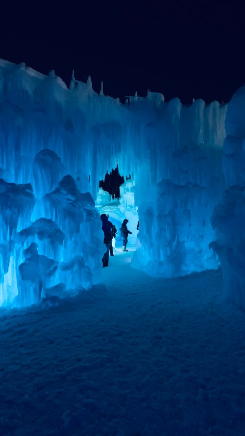 A glowing blue ice cave with people walking through, illuminated against a dark night sky.