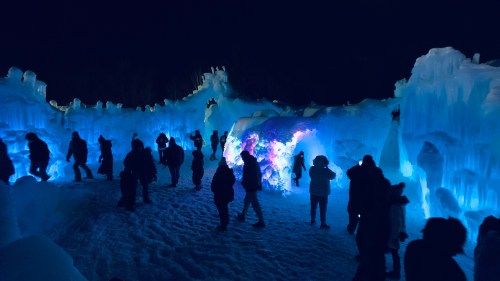 Visitors explore a stunning ice sculpture display illuminated in blue light at night.